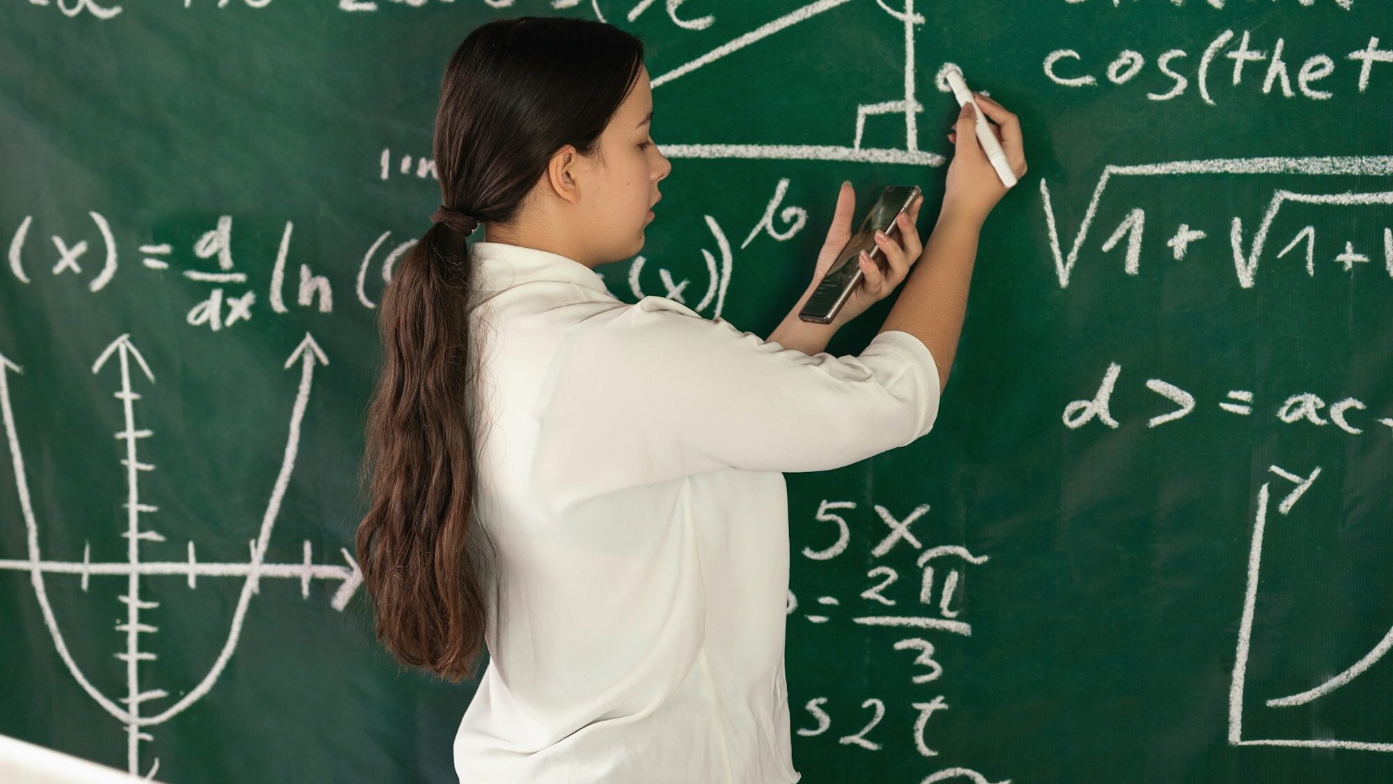 Girl writes mathematical examples on the school board. solves a geometry problem.